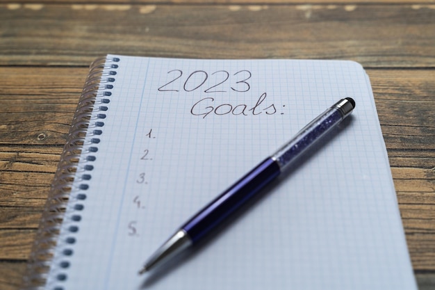 Foglio di taccuino scritto 2023 per mettere i propositi e gli obiettivi dell'anno con una penna e uno sfondo di legno
