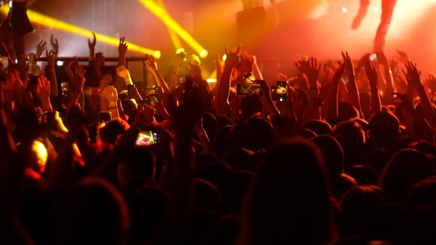 Folla energica di persone che ballano con le mani alzate all'illuminazione rossa del concerto rock