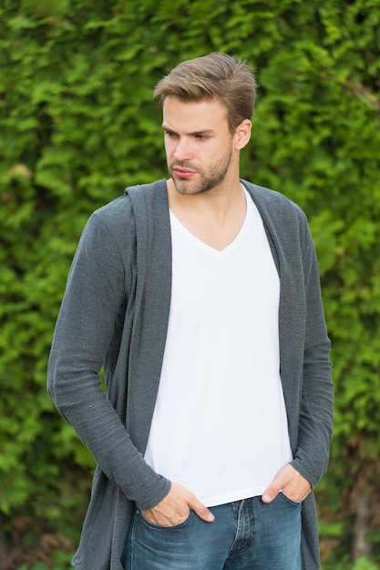 Fondamenti di una buona vestizione. Viso con la barba lunga dell'uomo bello e capelli biondi alla moda. Fondo di verde della natura dell'uomo caucasico bello. Stile casual da ragazzo barbuto. Servizio di barbiere. Bel macho.