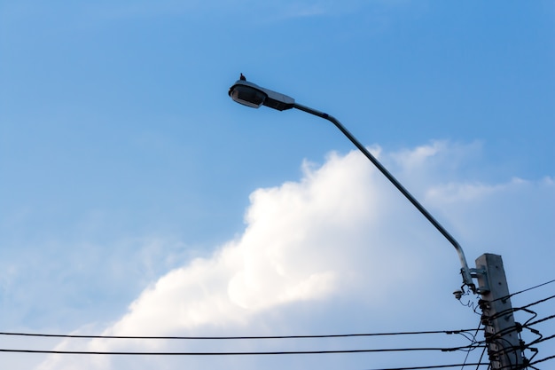 Fondo astratto nuvoloso cielo blu, palo nero della lampada e potere del cavo.