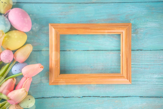 Fondo di festa di Pasqua e di primavera con i fiori del tulipano, uova pastello colorate sulla vista superiore del tavolo blu. Auguri di buona Pasqua.