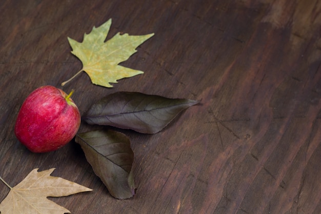 Fondo di legno di autunno con la mela e foglie gialle asciutte