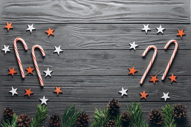 Fondo di legno grigio di Natale con abete, pigne, canna di Natale, stelle rosse e bianche