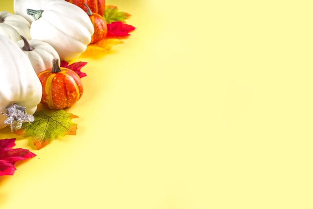 Fondo festivo di festa di giorno del ringraziamento. Zucche arancioni bianche, foglie autunnali colorate, bacche, su sfondo giallo colorato, vista dall'alto, cornice per la copia dello spazio