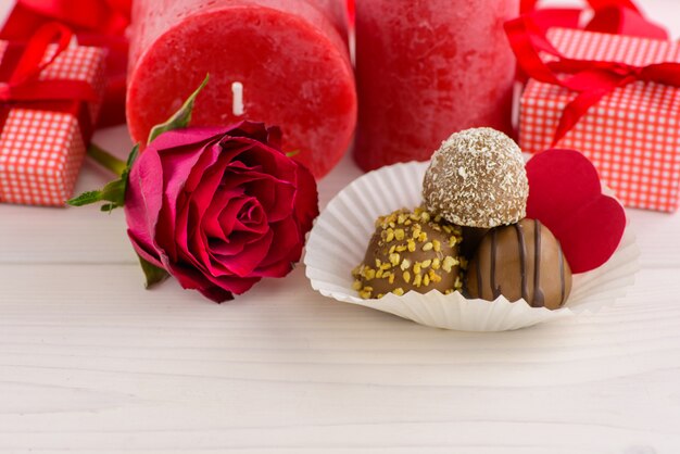 Fondo rosso di giorno di biglietti di S. Valentino con le rose rosse e cioccolato su una tavola di legno bianca.