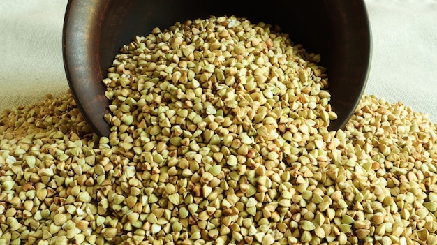 Fondo sparso del grano saraceno, grano saraceno verde crudo in una ciotola o un piatto marrone dell'argilla. Semole sane.