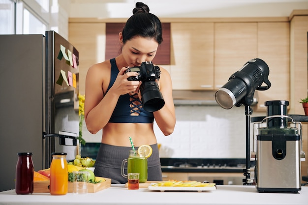 Food blogger che imposta attrezzature luminose professionali quando scatta foto di ingredienti per frullati verdi sul bancone della cucina