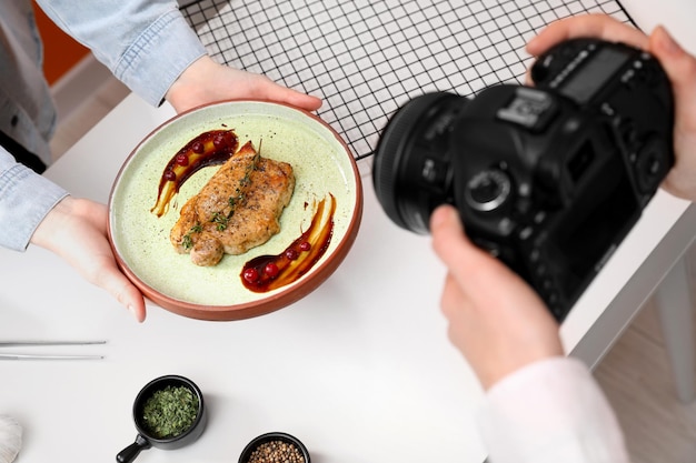 Food stylist che tiene il piatto con un delizioso medaglione di carne mentre il fotografo scatta foto in primo piano in studio