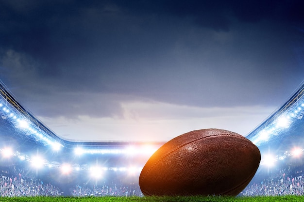 Football americano nello stadio di notte con riflettori e palla nella parte anteriore. Tecnica mista