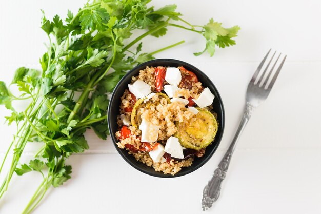 Forcella vicino a insalata di quinoa e verdure al forno con erbe su un tavolo bianco