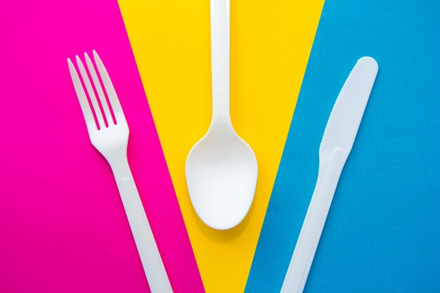 Forchetta, coltello e cucchiaio di plastica bianchi su sfondo multicolore. Utensile da cucina. Vista dall'alto. Stile minimalista. Copia, spazio vuoto per il testo