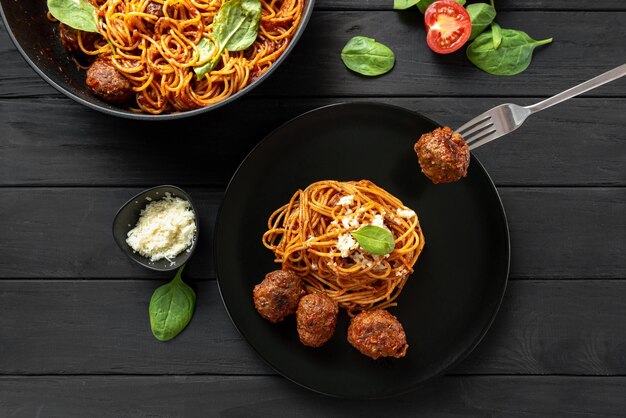 Forchetta con una polpetta pasta italiana in salsa di pomodoro e carne con basilico su un piatto nero su un legno