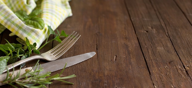 Forchetta e coltello vintage con erbe e tovagliolo su un vecchio tavolo di legno