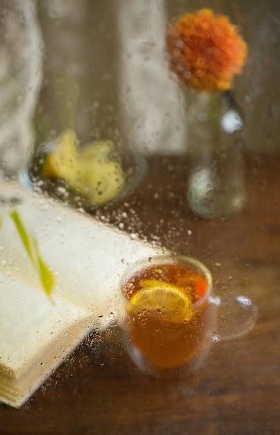 Forma autunnale Rami di betulla ingialliti attraverso una finestra piovosa bagnata Libro e tè al limone Comfort domestico in caso di maltempo