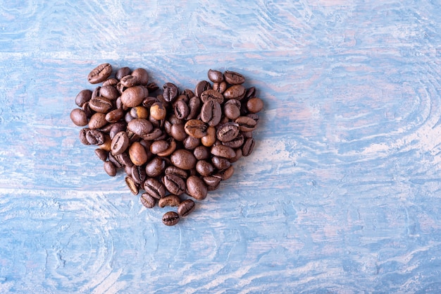 Forma di cuore fatta di chicchi di caffè su uno sfondo di legno elegante blu