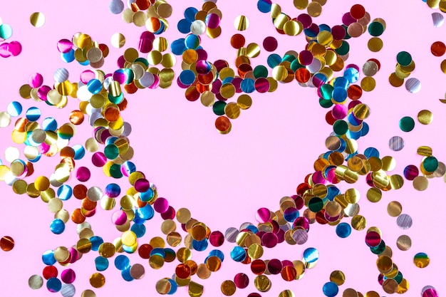 Forma di cuore fatta di confetti dorati colorati sullo sfondo rosa