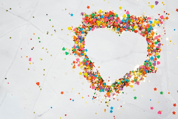 Forma di cuore fatta di piccole caramelle colorate su uno sfondo di marmo bianco giorno di San Valentino sull'amore