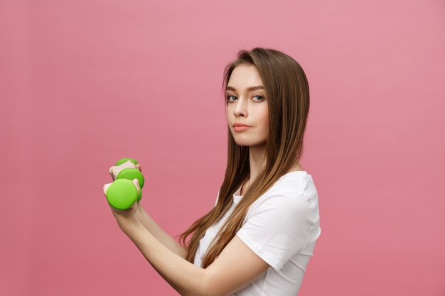 Forma fisica, giovane donna con i dumbbells alla priorità bassa dello studio. Isolato grazioso della ragazza sopra il rosa