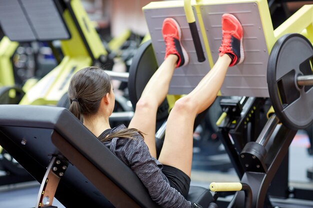 forma fisica, sport, culturismo, esercizio e concetto della gente - giovane donna che flette i muscoli sulla macchina della stampa della gamba in palestra