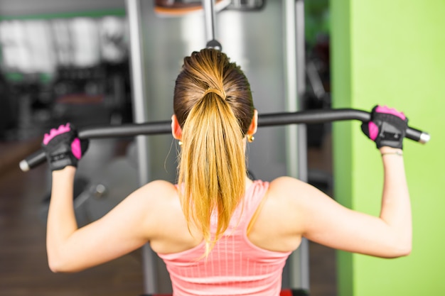 Forma fisica, sport, sollevamento pesi e concetto della gente - ragazza sportiva che sviluppa alcuni muscoli su un simulatore