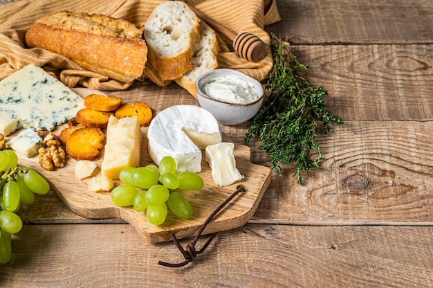 Formaggi assortiti Brie, Camembert, Roquefort, parmigiano, formaggio cremoso blu con uva, fichi, pane e noci. fondo in legno. Vista dall'alto. Copia spazio.