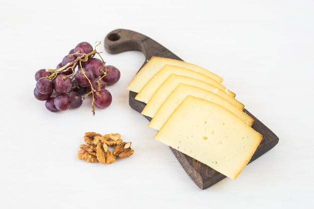 Formaggio a fette con uva e noci sul tavolo rustico.