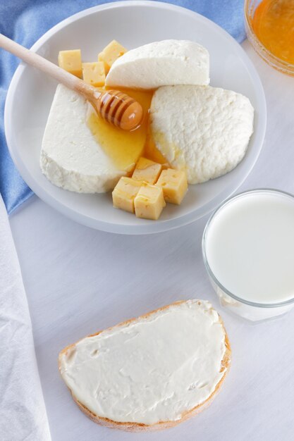 Formaggio a pasta dura giallo e brinza morbida bianca con miele su un piatto bianco su sfondo chiaro Primo piano di prodotti lattiero-caseari