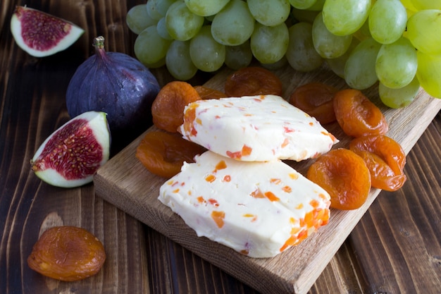 Formaggio a pasta molle con albicocche secche e frutta sul tagliere di legno