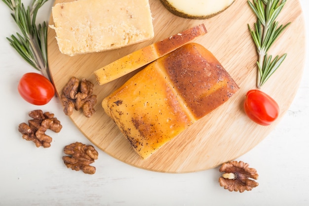 Formaggio affumicato e vari tipi di formaggio con rosmarino e pomodori su tavola di legno su una superficie di legno bianca