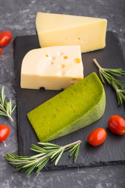 Formaggio al basilico verde e vari tipi di formaggio con rosmarino e pomodori sul bordo dell'ardesia nera su una superficie di cemento nero