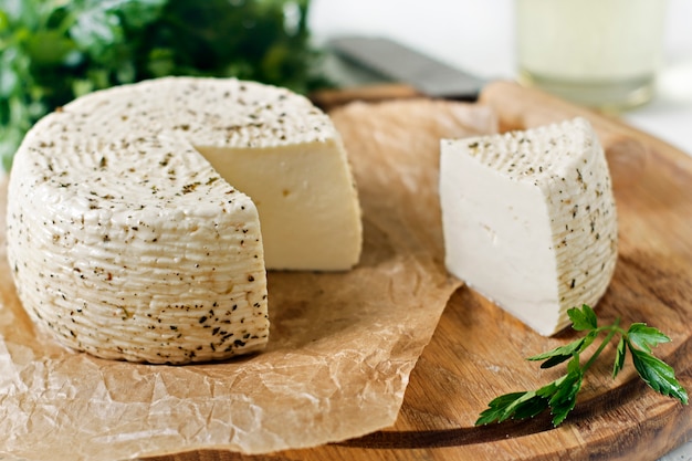 Formaggio bianco su una tavola di legno su uno sfondo bianco con verdi