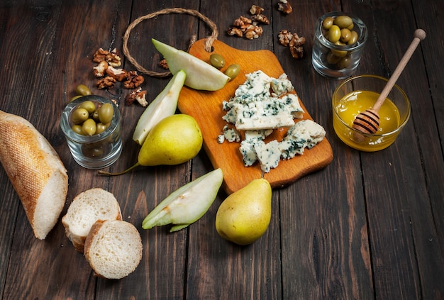 Formaggio blu con miele, olive e pere sul tavolo rustico.