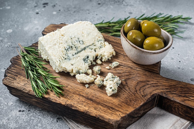 Formaggio blu danese su una tavola di legno con olive e rosmarino. Sfondo grigio. Vista dall'alto.