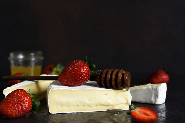 Formaggio Brie con fragole e miele su un tavolo da cucina nero. Spuntino. Messa a fuoco orizzontale.