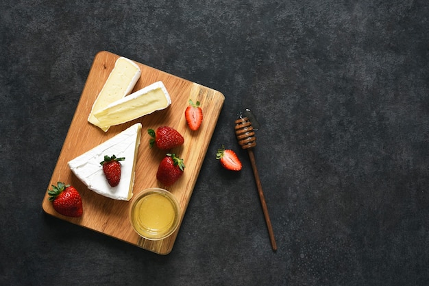 Formaggio Brie con fragole e miele su un tavolo da cucina nero. Vista dall'alto. Spuntino.