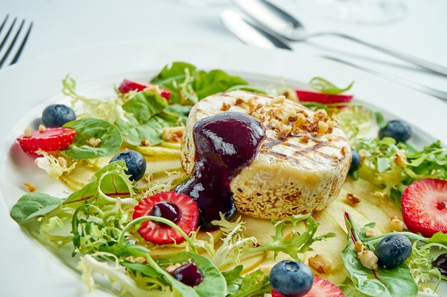 Formaggio camembert alla griglia con mele, fragole e mirtilli in un piatto bianco sul piatto bianco