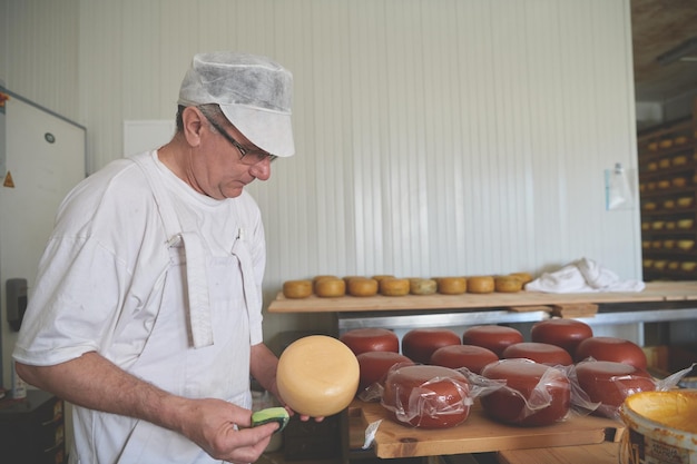 Formaggio che prepara forme di formaggio di capra e di vacca durante il processo di stagionatura in una fabbrica di produzione alimentare locale