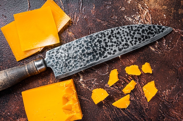 Formaggio Cheddar affettato su un tavolo da cucina con un coltello. tavolo scuro. Vista dall'alto.