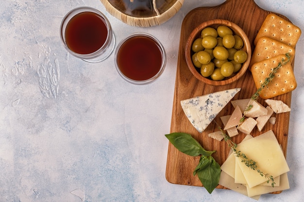 Formaggio, cracker, olive sul tagliere e bicchieri da vino rosso