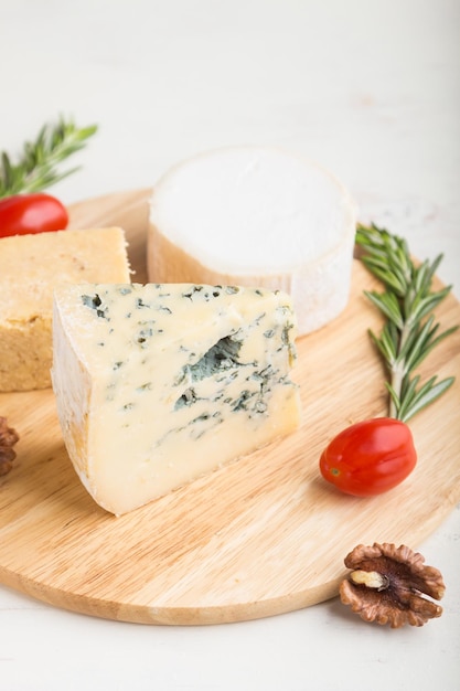 Formaggio erborinato e vari tipi di formaggio con rosmarino e pomodori su tavola di legno su fondo di legno bianco. Vista laterale, primo piano, messa a fuoco selettiva.