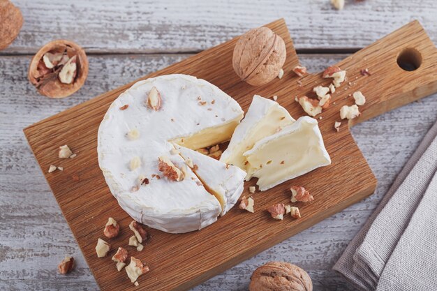 Formaggio francese a pasta molle di camembert servito con noci tritate su piatto di legno.