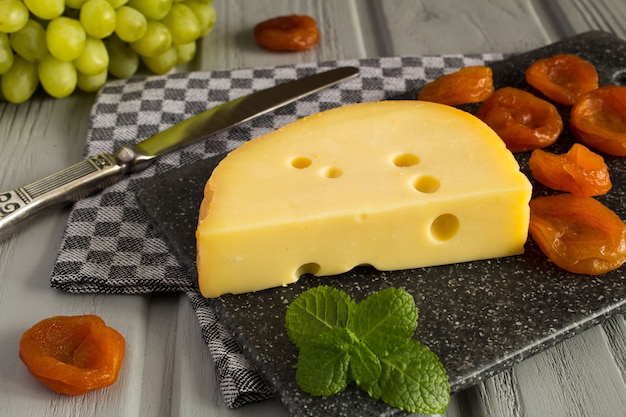 Formaggio giallo e albicocche secche sul legno grigio