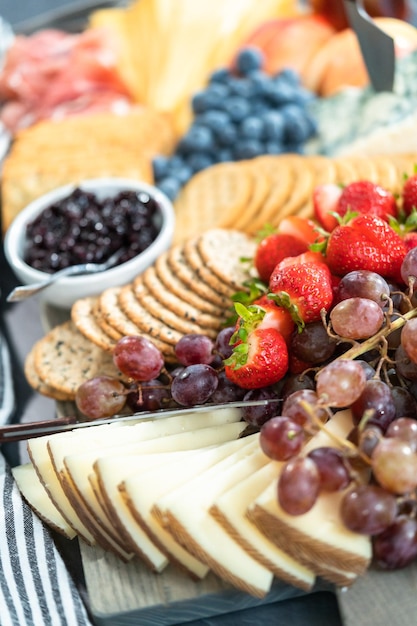 Formaggio gourmet, cracker e frutta su un tagliere di legno serviti come antipasto.