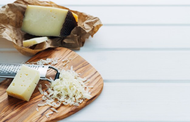 Formaggio grattugiato con grattugia e un pezzo di formaggio sul bordo della cucina. Concetto di cucina.