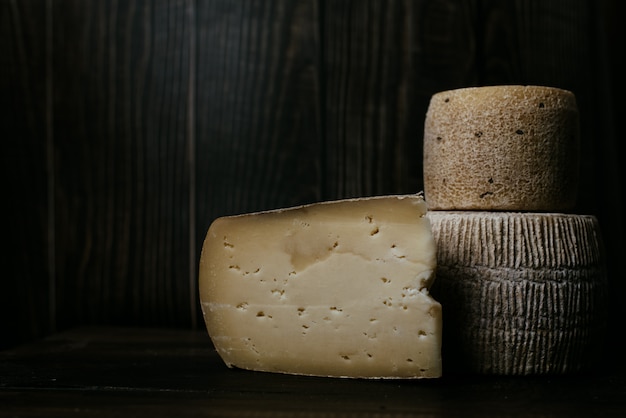 Formaggio Manchego accanto a gorgonzola e kravot su una tavola di legno scuro. Fotografia di formaggi in chiave di basso. Formaggio a pasta molle naturale prodotto con latte di mucca e capra