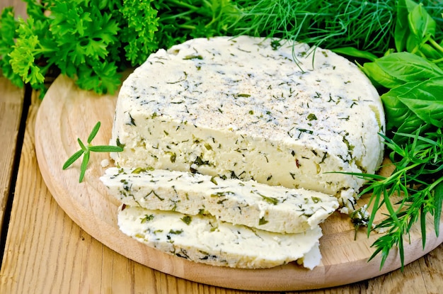 Formaggio rotondo fatto in casa con erbe e spezie tagliato a fette su una tavola di legno