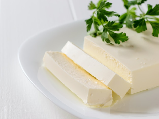 Formaggio serbo con prezzemolo su un piatto bianco su un tavolo bianco. La vista dall'alto. Prodotto lattiero-caseario.