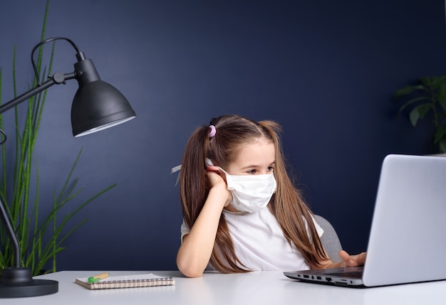 Formazione online a distanza. studentessa in maschera medica studiando a casa, lavorando sul portatile e facendo i compiti a scuola. concetto di quarantena di coronavirus
