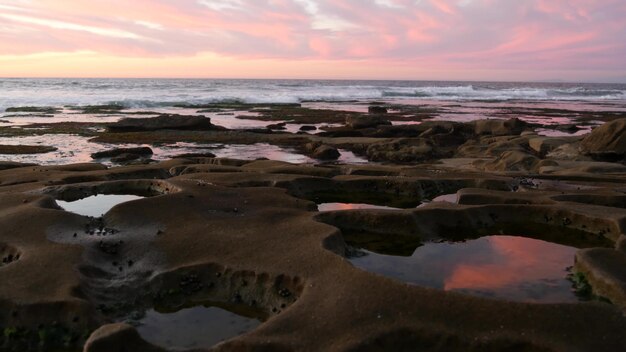 Formazione rocciosa della piscina di marea erosa nella riflessione del cielo di tramonto della California nell'acqua