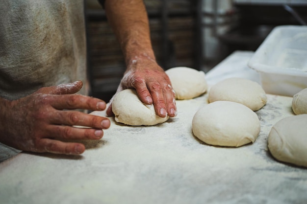 Fornaio anonimo che preforma l'impasto del pane in panetteria Lo sta impastando